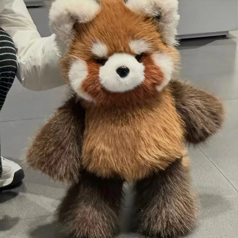 A plush red panda toy being held by a person, shown against a gray indoor floor background.