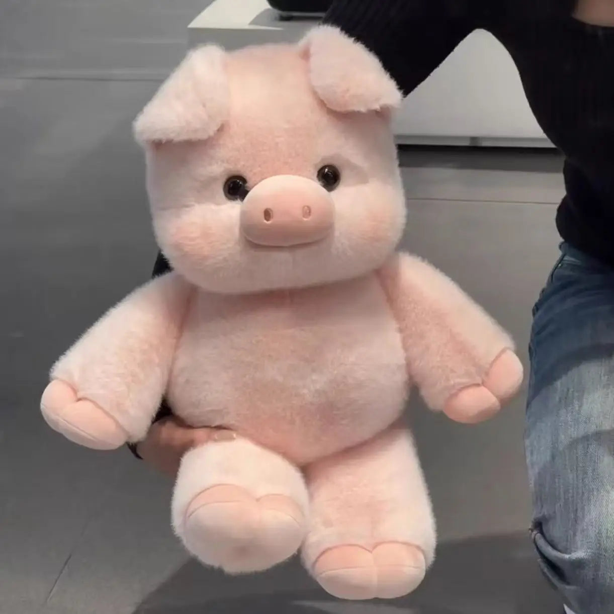 Pink plush pig toy held by a person on a reflective surface with a neutral background